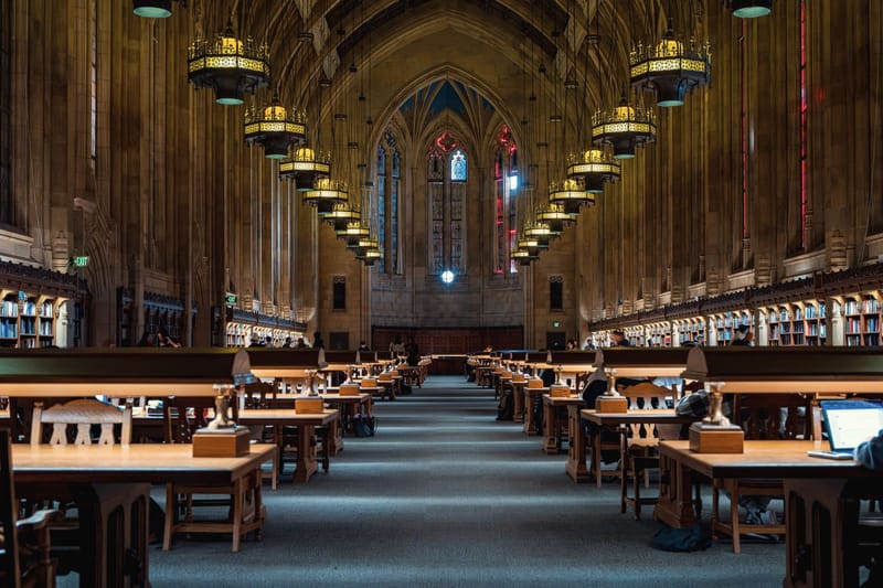 A long, vaulted university reading room lined with study tables and lamps.