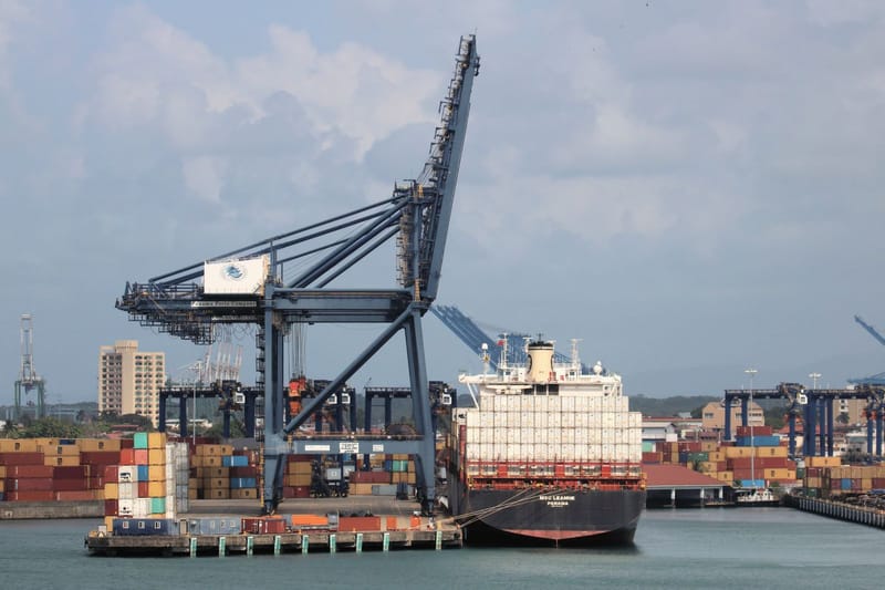 A container ship under cranes at a busy seaport.
