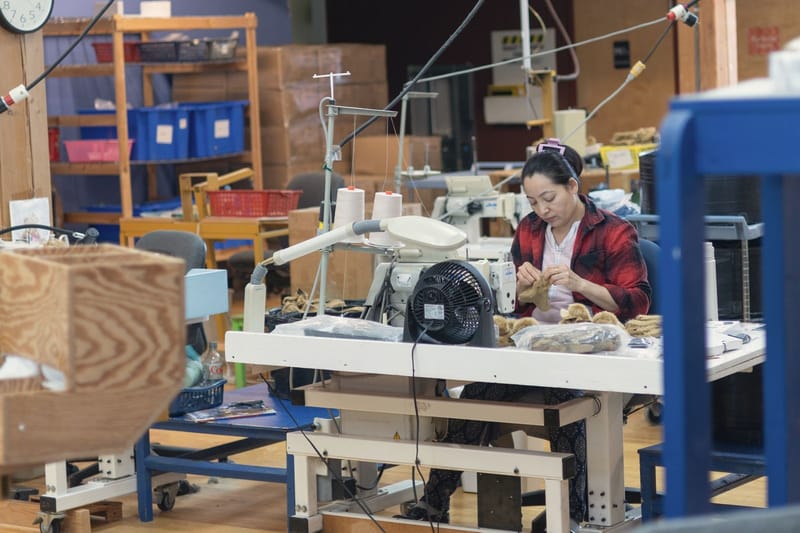 A worker sews at a machine in a busy workshop.